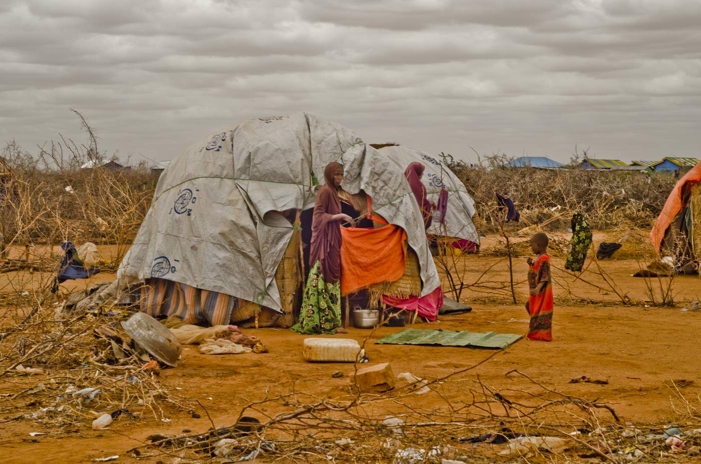 Mother beckoning her child to enter their shelter made of wood and plastic sheeting in Airstrip Area Displacement Site, Dolo Ado, Somali Region. Photo: Rikka Tupaz\/UN Migration Agency (IOM) 2017